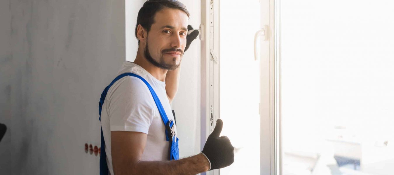 Male repairer in overalls installs a window and showing thumb